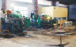 Cold forging: green forging machines fed with steel wire from a coil, with forged parts heaped on the floor.