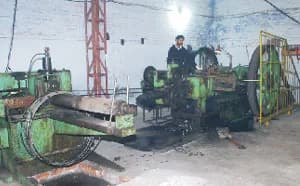 Cold header: a heading machine fed with steel wire from a large coil, with its operator beside it.