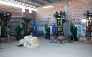 Hot forging section: a row of forging presses along a brick wall, with operators at work and sacks of parts on the floor.